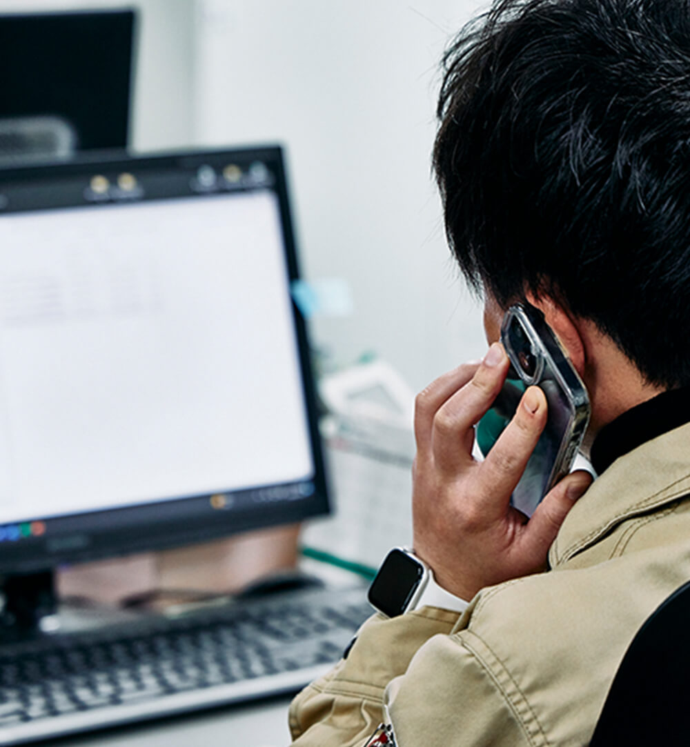 デスクワークをしながらスマートフォンで電話をしている男性