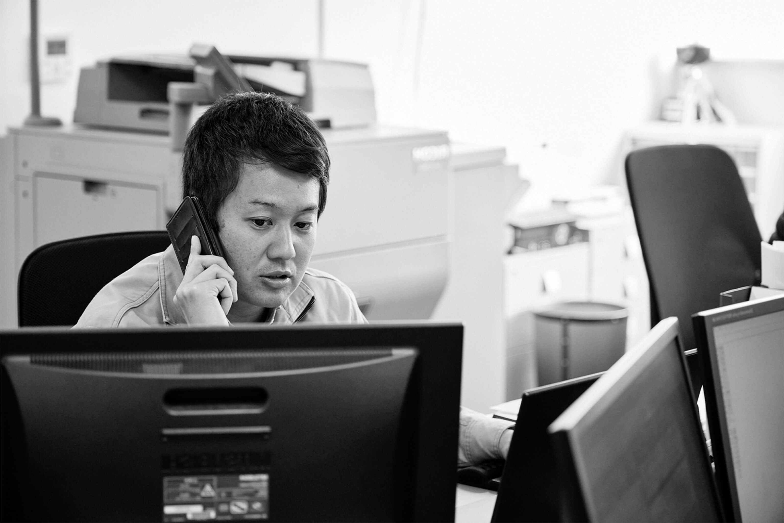 デスクに座ってスマートフォンで電話をしている男性